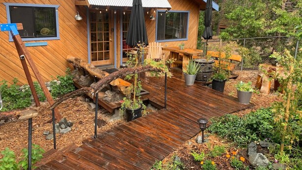 A wooden cabin with a deck, surrounded by greenery and plants. - Wheelchair Access, Near Ski & Snow Play, Pets OK! (Wrightwood)