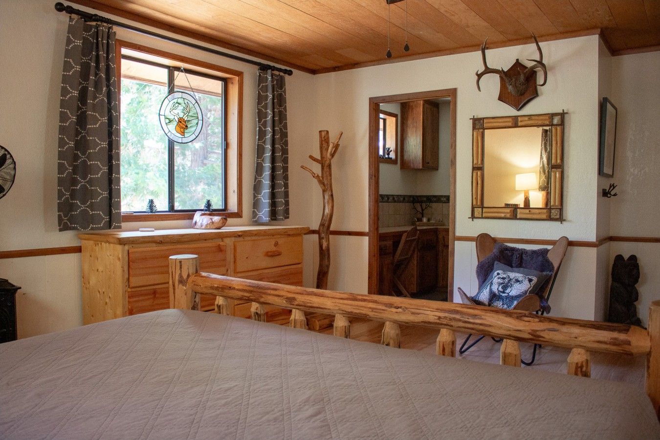 Une chambre à coucher rustique avec un lit en bois, une commode, un miroir et une fenêtre avec des rideaux.