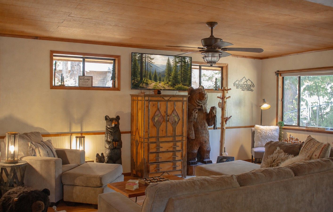 A cozy living room with a wooden ceiling, a ceiling fan, a large window, and a bear statue.
