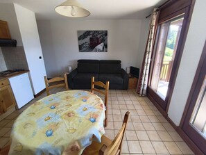 A dining area with a table covered in a tablecloth, a sofa, a television, and a painting on the wall.