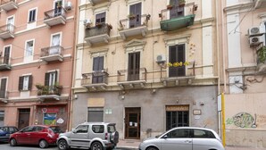 A row of parked cars along a street with a building featuring multiple balconies and a sign that reads 'ArtigianArte.' - GuestHost - Cozy apartment equipped with all comforts and able to accommodate up to 4 people. The flat is located in a very central position: we are in fact a 10-minute walk from Piazza Maria Immacolata, just over 15 minutes from the Archaeological Museu (Taranto)