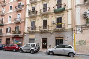A row of parked cars along a street with a building featuring multiple balconies and a sign that reads 'ArtigianArte.' - GuestHost - Cozy apartment equipped with all comforts and able to accommodate up to 4 people. The flat is located in a very central position: we are in fact a 10-minute walk from Piazza Maria Immacolata, just over 15 minutes from the Archaeological Museu (Taranto)