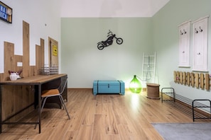 A room with a wooden desk, a blue storage box, a wall-mounted motorcycle decoration, a green lamp, and a rack with hooks.