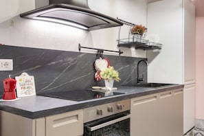 A modern kitchen with a black marble countertop, stainless steel appliances, and a small plant on the sink.