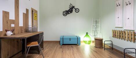Et værelse med et træskrivebord, en blå opbevaringskasse, en motorcykelpynt på væggen, en grøn lampe og et stativ med kroge.