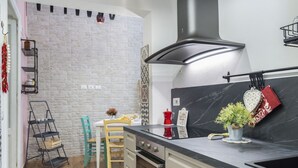 A kitchen with a white brick wall, a black stove, and a wooden dining table. - GuestHost - Cozy apartment equipped with all comforts and able to accommodate up to 4 people. The flat is located in a very central position: we are in fact a 10-minute walk from Piazza Maria Immacolata, just over 15 minutes from the Archaeological Museu (Taranto)