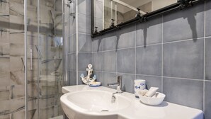 A bathroom with a glass shower enclosure, a white sink with a mirror above it, and a tiled wall. - GuestHost - Cozy apartment equipped with all comforts and able to accommodate up to 4 people. The flat is located in a very central position: we are in fact a 10-minute walk from Piazza Maria Immacolata, just over 15 minutes from the Archaeological Museu (Taranto)