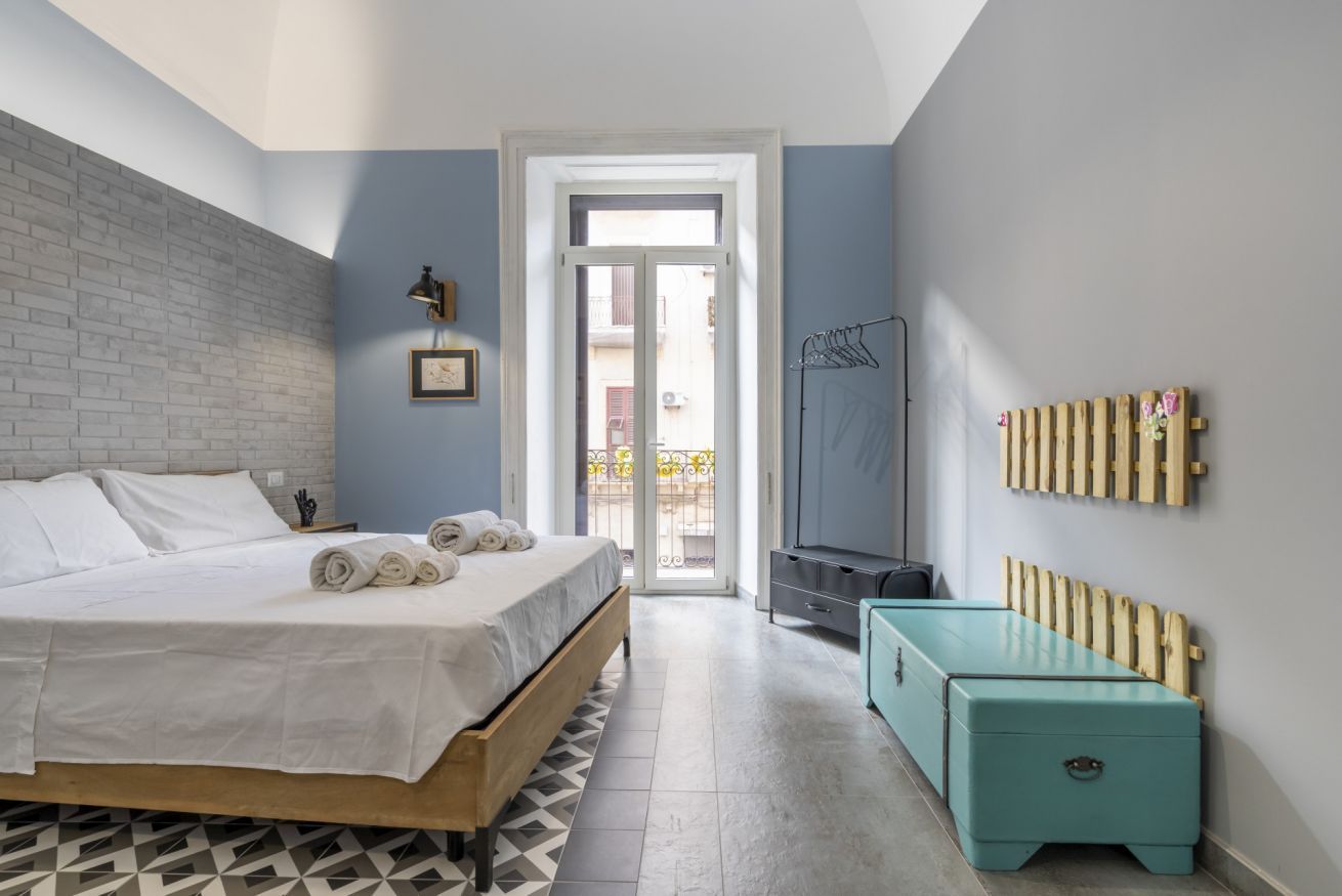Un dormitorio con cama, un banco de madera, un radiador y vistas a través de una puerta.