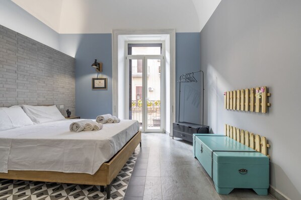 Un dormitorio con cama, un banco de madera, un radiador y vistas a través de una puerta.
