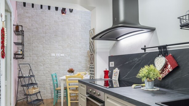 A kitchen with a white brick wall, a black stove, and a wooden dining table. - GuestHost - Cozy apartment equipped with all comforts and able to accommodate up to 4 people. The flat is located in a very central position: we are in fact a 10-minute walk from Piazza Maria Immacolata, just over 15 minutes from the Archaeological Museu (Taranto)