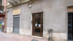 A building with a closed metal shutter door, a glass door entrance, and a visible sign on the wall. - GuestHost - Cozy apartment equipped with all comforts and able to accommodate up to 4 people. The flat is located in a very central position: we are in fact a 10-minute walk from Piazza Maria Immacolata, just over 15 minutes from the Archaeological Museu (Taranto)