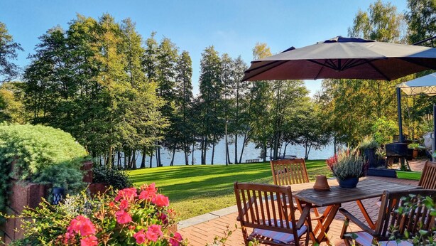 Une terrasse extérieure avec une table et des chaises, entourée d’une pelouse bien entretenue et d’arbres.
