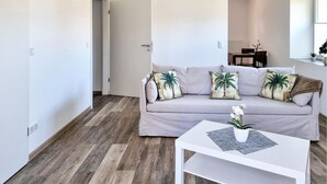 Un salon moderne avec un canapé gris clair, deux coussins décoratifs, une table basse blanche et un plancher en bois.
