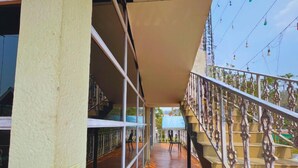 A corridor with a wooden floor, a staircase with ornate railings, and a view of a building in the distance. - Chang's Resort (Guwahati)