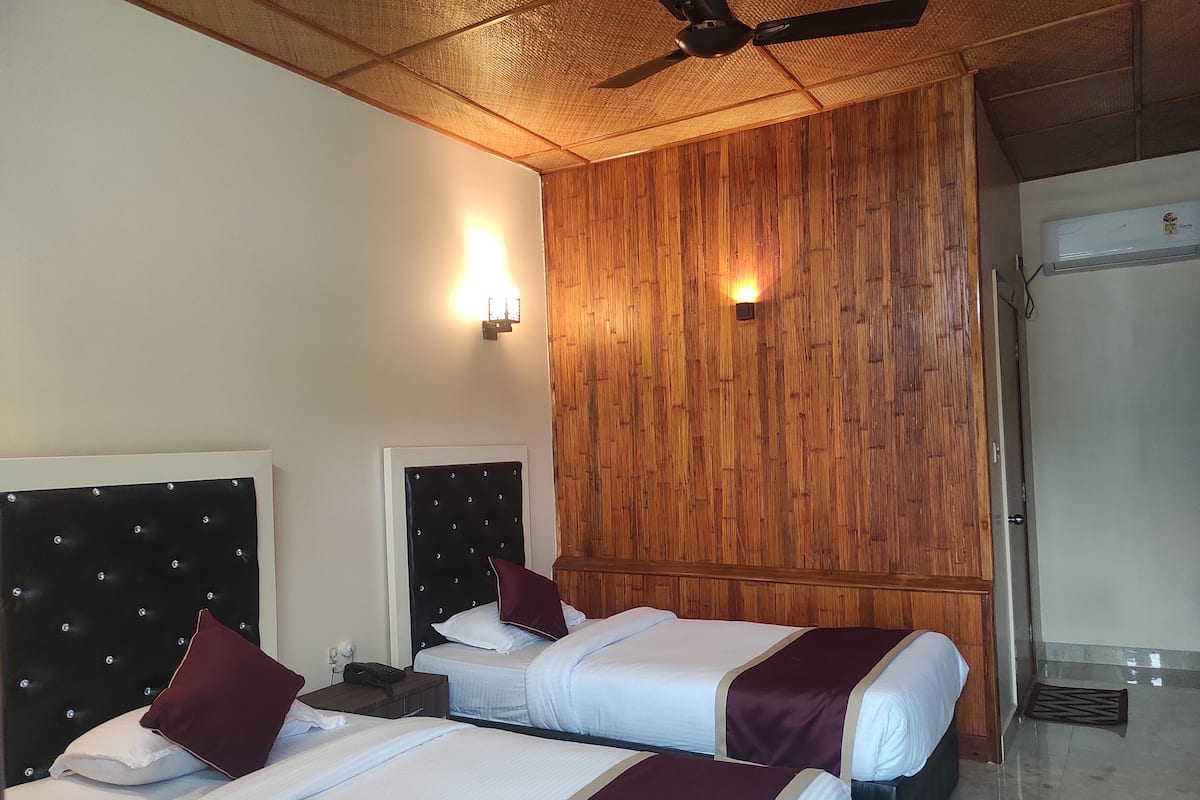 A hotel room with two beds, a wooden panel wall, a ceiling fan, and a bathroom door.