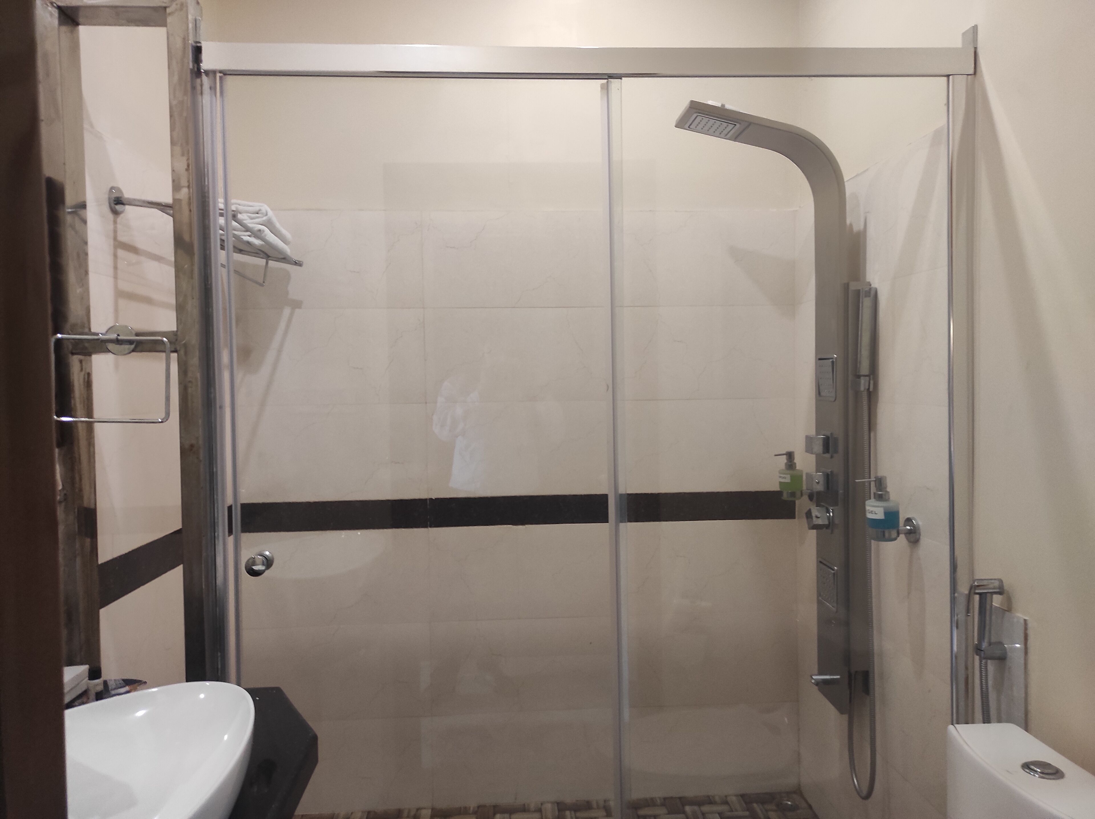 A glass-enclosed shower with a handheld showerhead, a towel rack, and a soap dispenser.