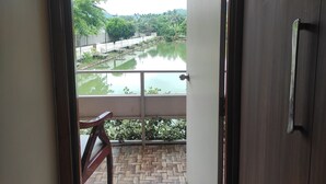 A room with a view of a water body, a wooden chair, and a door. - Chang's Resort (Guwahati)