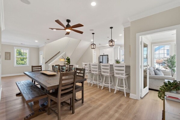 A dining area with a wooden table and chairs, a ceiling fan, pendant lights, and a view to a living area. - Luxury Sandbridge Retreat | Pool, Hot Tub, Game Room, Walk to Beach SP305 (Virginia Beach)
