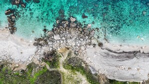 An aerial view of a beach with clear turquoise waters, rocky formations, and a sandy shoreline.
