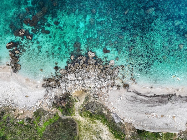 An aerial view of a beach with clear turquoise waters, rocky formations, and a sandy shoreline.