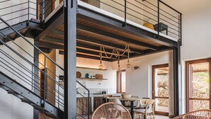A spacious living area with a modern staircase, wicker furniture, and a glass coffee table.