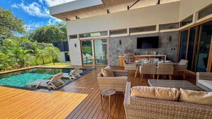A modern outdoor living area with a pool, wicker furniture, and a built-in kitchen. - Casa Dos Playas, private pool with direct access to 2 beaches! (Tamarindo)