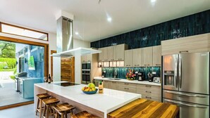 A modern kitchen with a large island, wooden stools, stainless steel appliances, and a view of the outdoors. - Casa Dos Playas, private pool with direct access to 2 beaches! (Tamarindo)