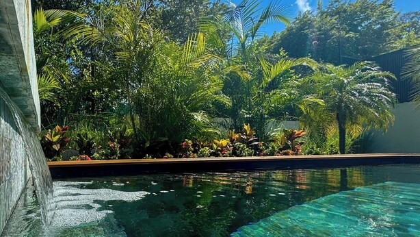 A clear swimming pool surrounded by lush tropical vegetation and a wooden deck. - Casa Dos Playas, private pool with direct access to 2 beaches! (Tamarindo)