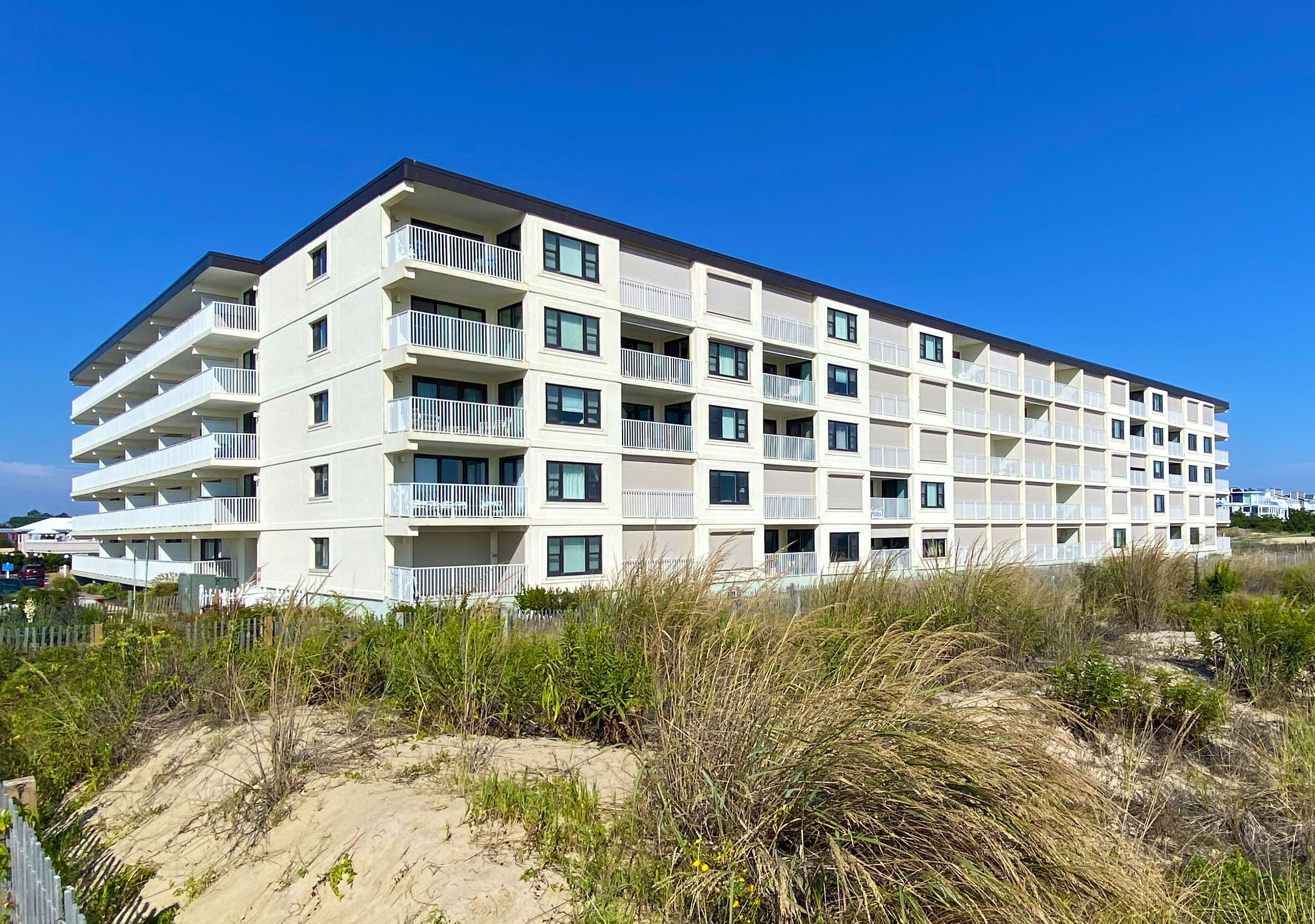 Ein mehrstöckiges Hotel mit Balkonen in der Nähe eines Strandes mit Dünen.