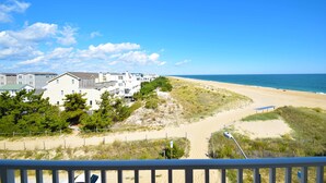 Une vue sur la plage, avec un sentier menant à une zone sablonneuse, entourée de verdure et de bâtiments.