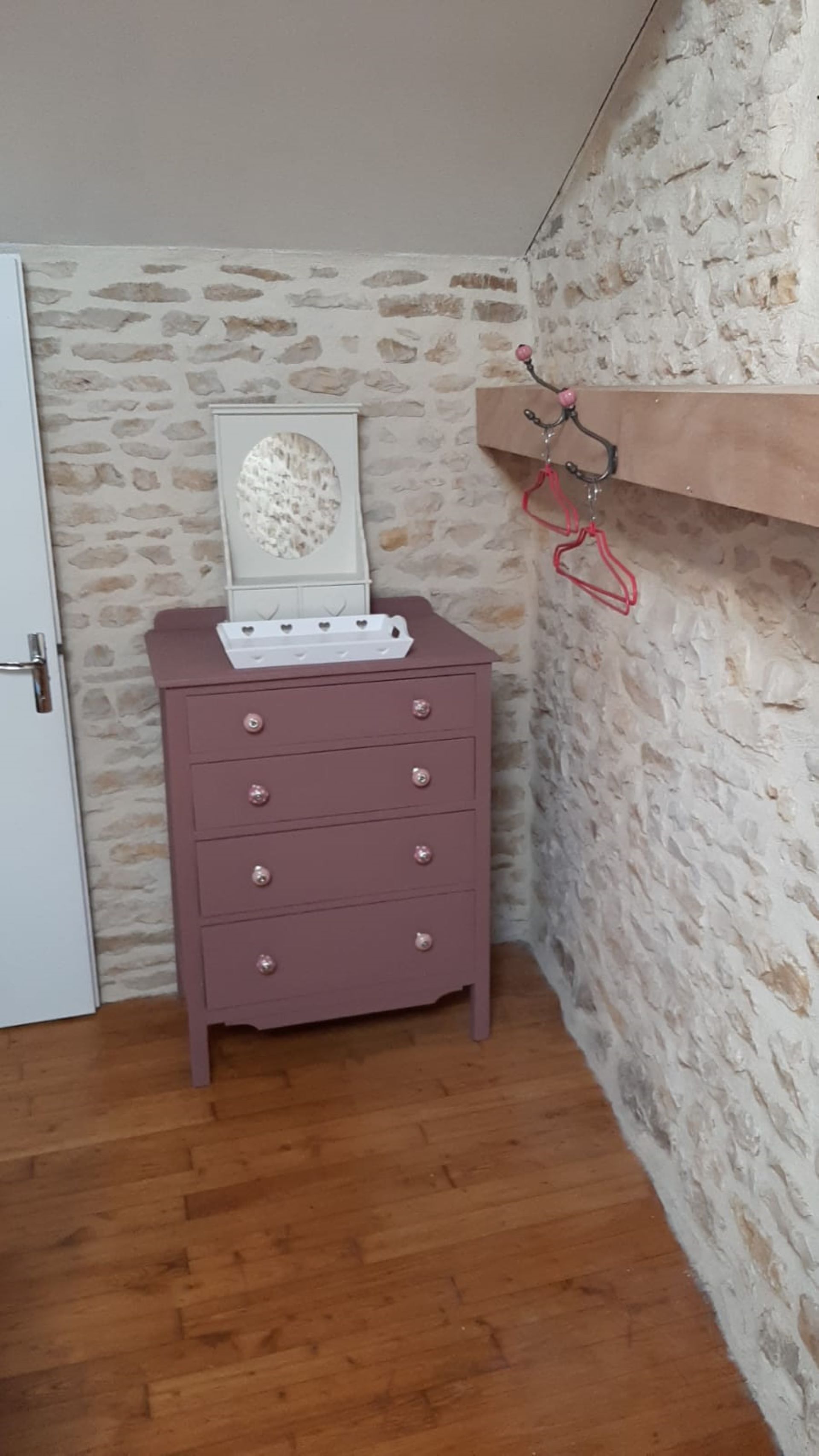 Una habitación de esquina con un aparador de madera, una pared de piedra y una estantería de madera con perchas rojas.