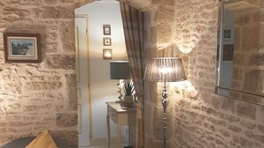 Un salon chaleureux avec des murs en pierre, un canapé gris agrémenté de coussins à carreaux, une petite table avec une lampe et un tableau encadré au mur.