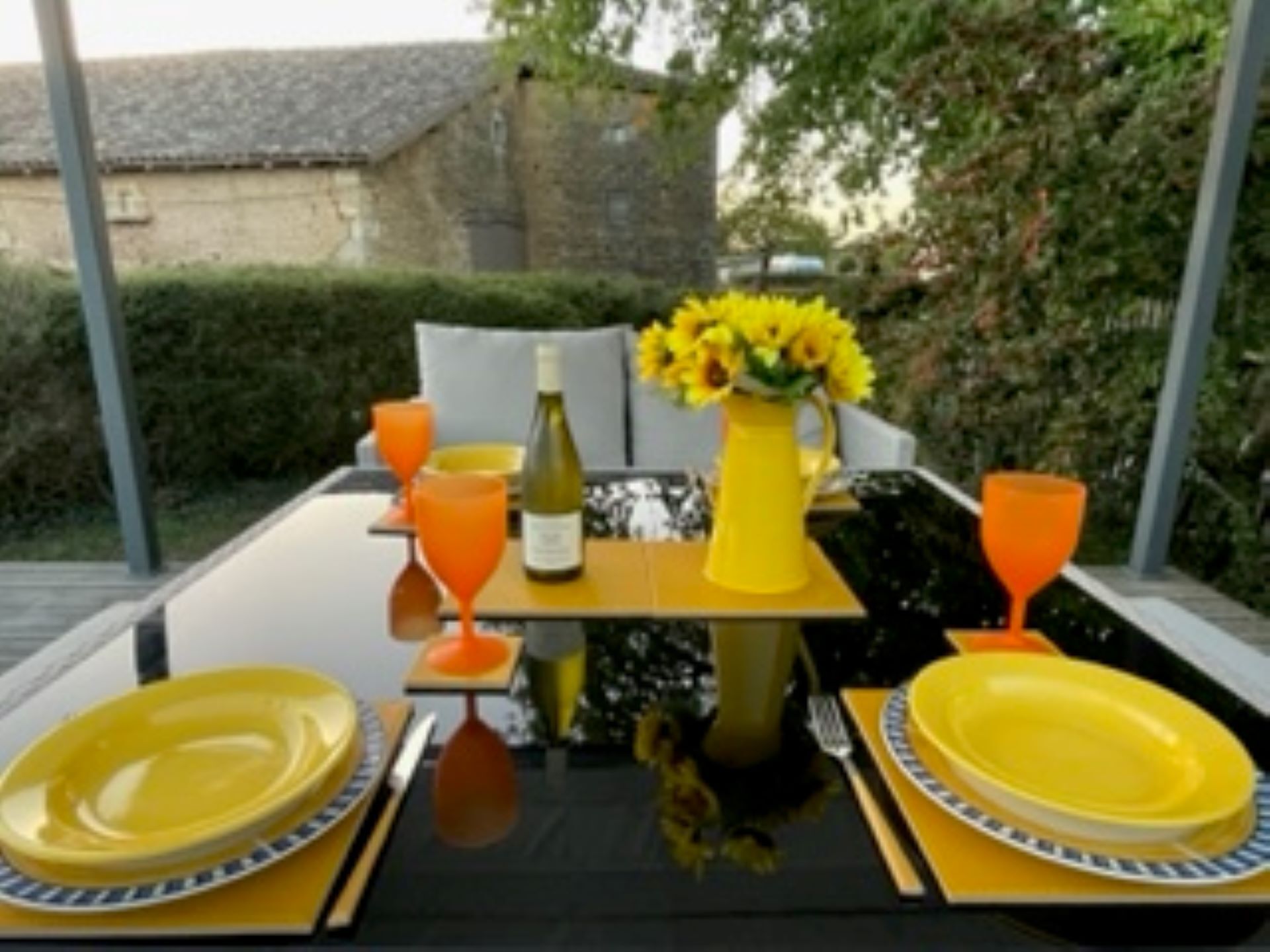 A table set for two with yellow plates, a yellow pitcher, and a bottle of wine.