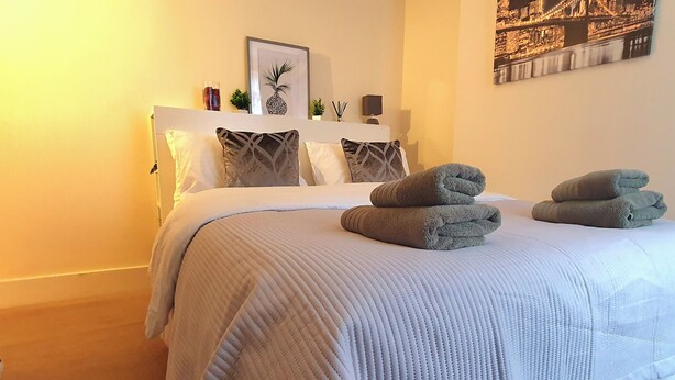 A neatly made bed with a white headboard, two rolled towels, and a framed picture above it. - Inviting 2-bed Cottage in Windsor (Windsor)