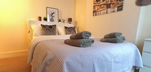 A neatly made bed with a white headboard, two rolled towels, and a framed picture above it. - Inviting 2-bed Cottage in Windsor (Windsor)