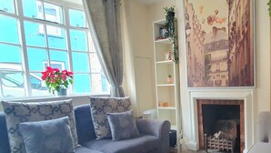 A living room with a sofa, a fireplace, a window with curtains, and a bookshelf. - Inviting 2-bed Cottage in Windsor (Windsor)