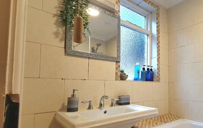 Un baño con un lavabo blanco, dos llaves, un espejo y una ventana con vistas al exterior.