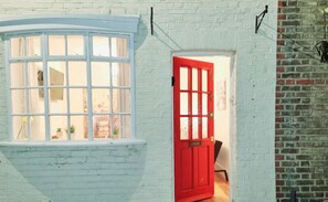 Un edificio de ladrillo blanco con una puerta roja y un ventanal saliente.