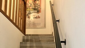Una scala con gradini in legno e un corrimano nero che conduce a una stanza con un poster appeso al muro.