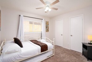 A bedroom with a single bed, a ceiling fan, a window with blinds, a door, and a bedside table with a lamp. - Lovely 3-bed House Perfect for Groups or Families (San Antonio)