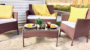 A patio area with wicker furniture, including two chairs and a table. There are plates with food and drinks on the table. - Lovely 3-bed House Perfect for Groups or Families (San Antonio)