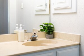 A bathroom with a beige sink, a mirror, a potted plant, and toiletries. - Lovely 3-bed House Perfect for Groups or Families (San Antonio)