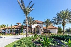 A residential house with a tiled roof, arched entrance, and surrounded by palm trees and landscaped gardens.
