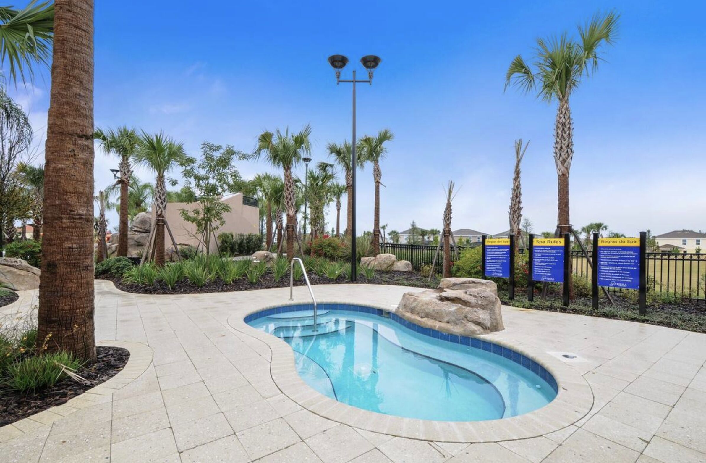 A swimming pool with a tiled edge, surrounded by palm trees and a paved walkway.