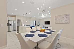 A modern kitchen with white cabinets, a stainless steel refrigerator, and a dining area with a white table and blue placemats.