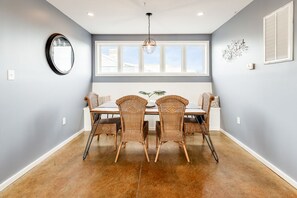 Un coin repas comprenant une table et quatre chaises, une grande fenêtre avec des stores et un luminaire suspendu.
