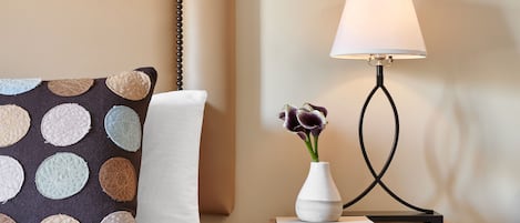 A neatly made bed with a patterned pillow, a bedside table with a lamp, and a vase with flowers.