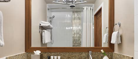 Ein Badezimmer mit Granitplatte, Waschbecken, Spiegel mit Holzrahmen und Duschbereich mit Glastür.