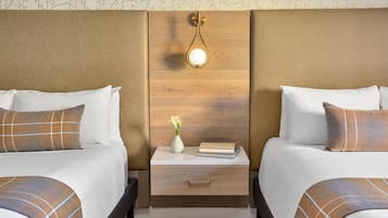 A hotel room with two beds, a bedside table with a lamp, and a small vase with flowers.