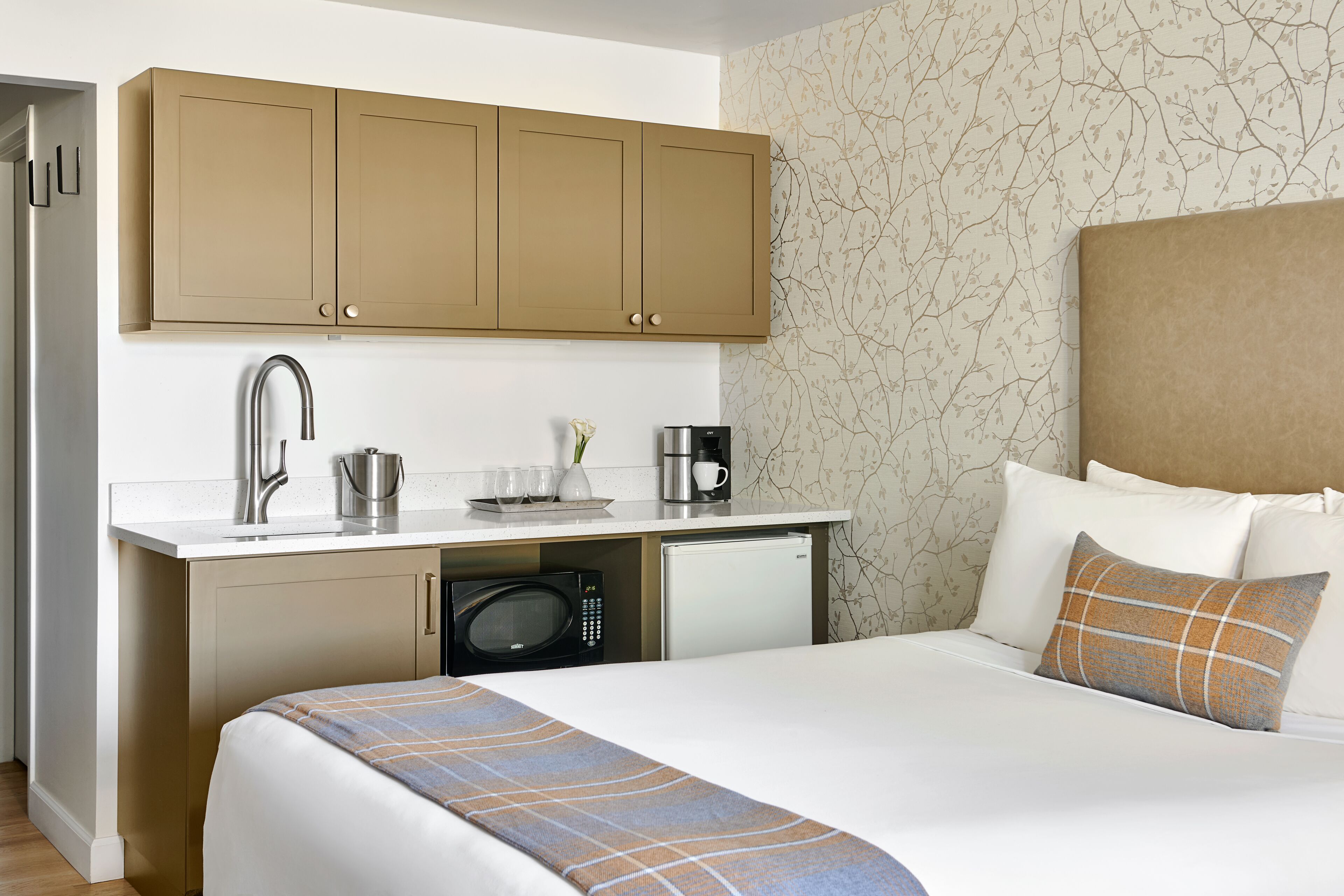 A hotel room with a bed, a small kitchenette with a microwave, a coffee maker, and a sink.